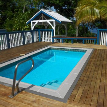 In-ground swimming pool on a wooden sun deck with a white gazebo and lush tropical greenery in Niue.