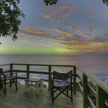 Sunset over the ocean as viewed from an outdoor deck seating area at a tropical accommodation.